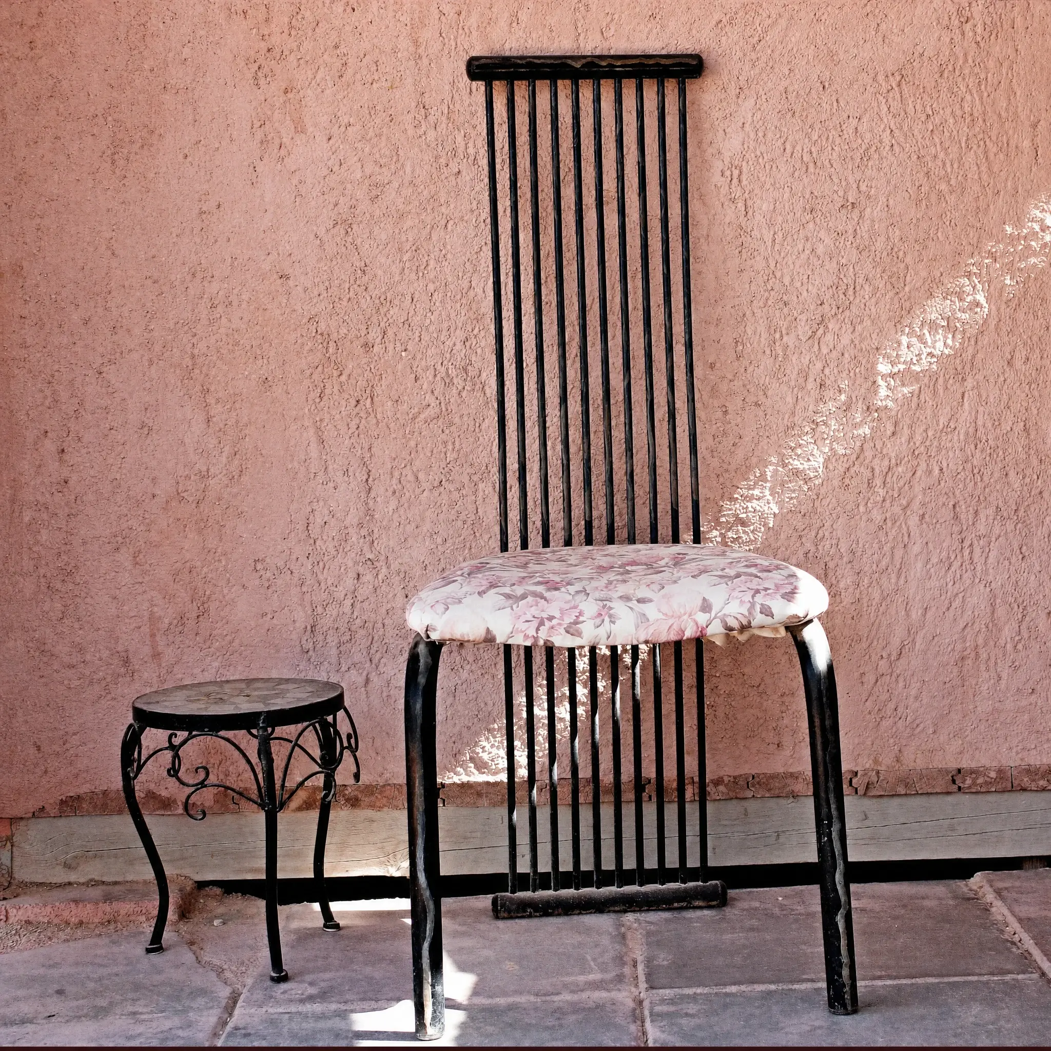 A metal chair with an embroidered seat against a pink wall
