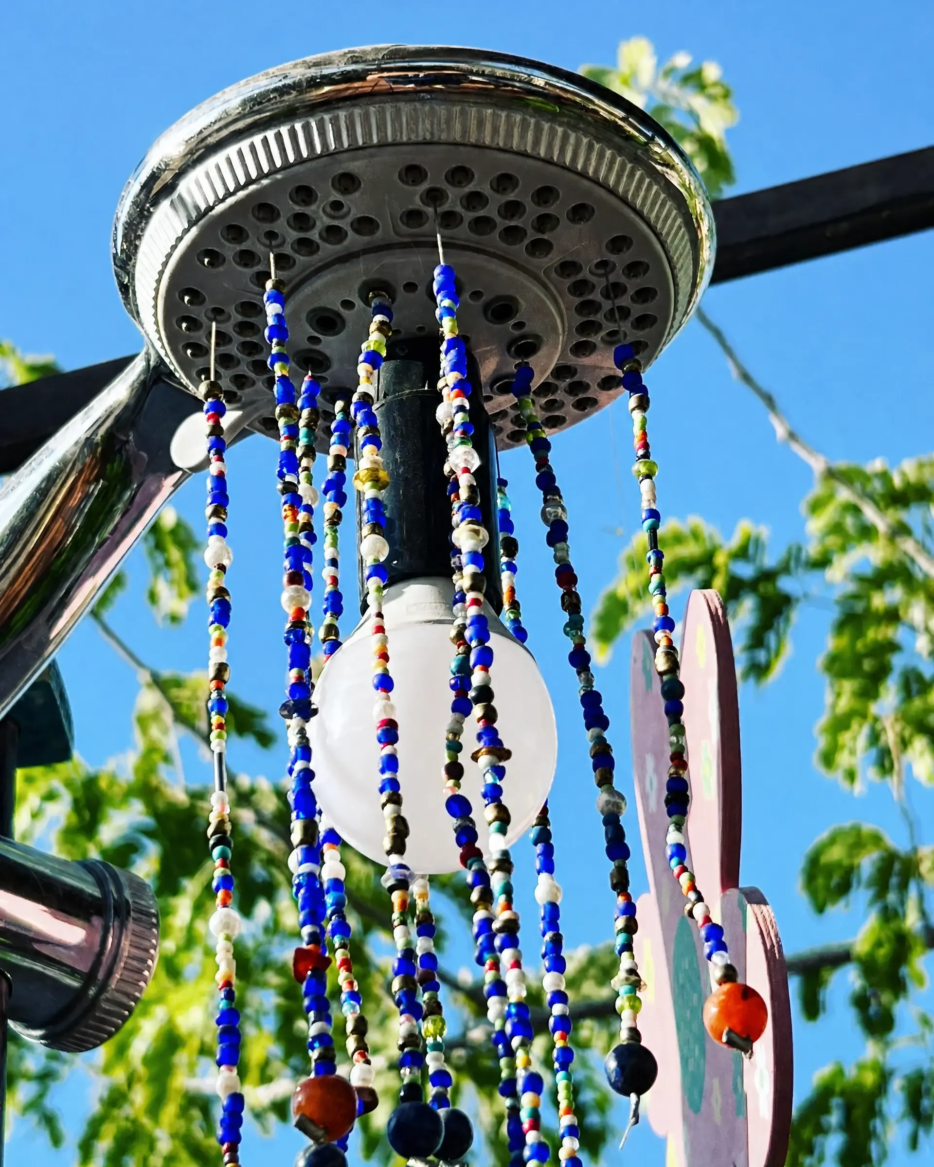 A wind chime of beads hung from an old shower head