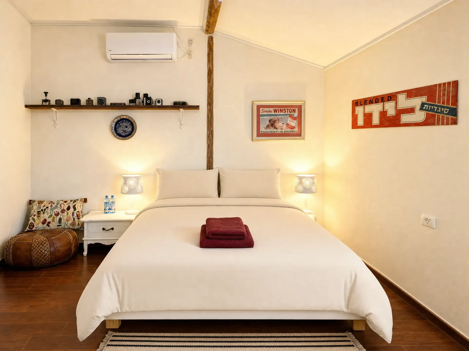 The Eden room: a double bed with light beige linens, bedside lamps, a shelf of cameras and old advertising signs
