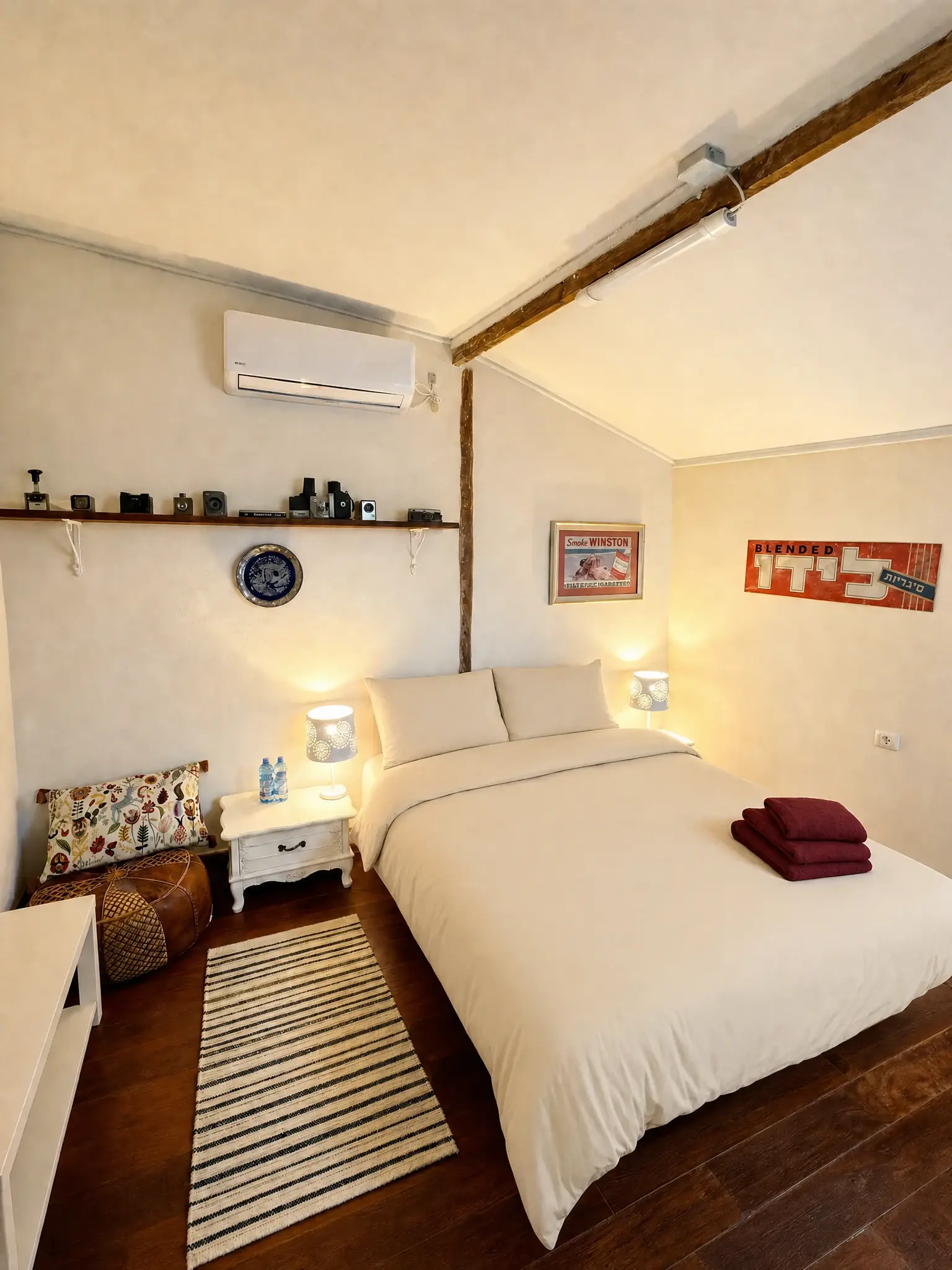 The Eden room by lamplight: a double bed, a white nightstand, a shelf of cameras and old advertising signs