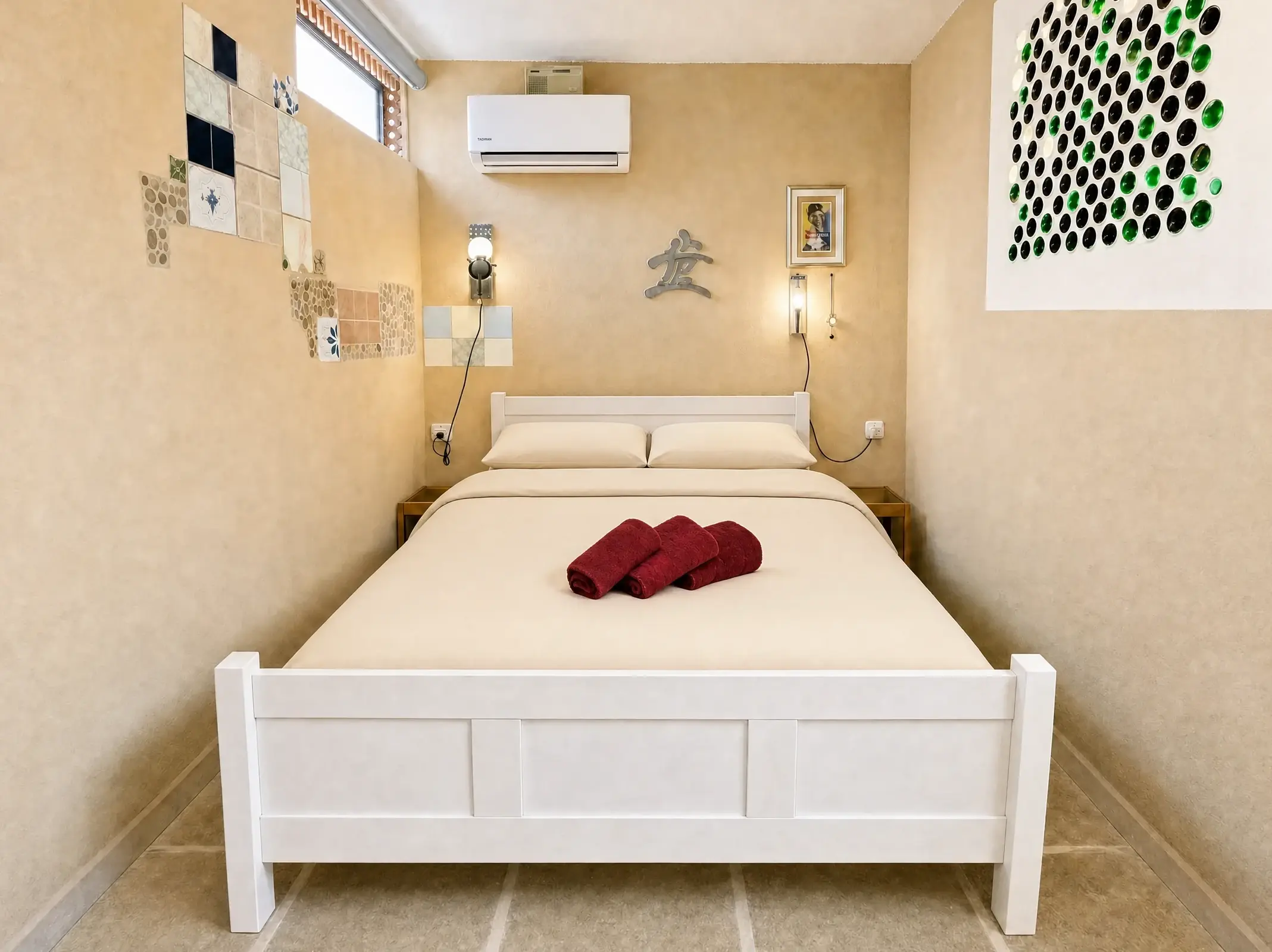 The Maayan room: a white double bed with light beige linens and towels, and bottle art on the wall