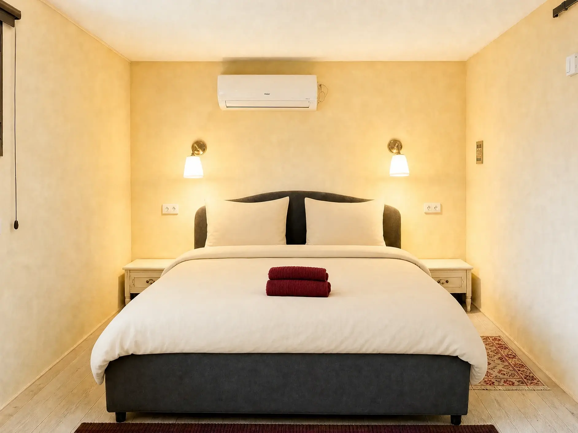 The Raz room: a double bed with light beige linens, two wall lamps and a striped rug