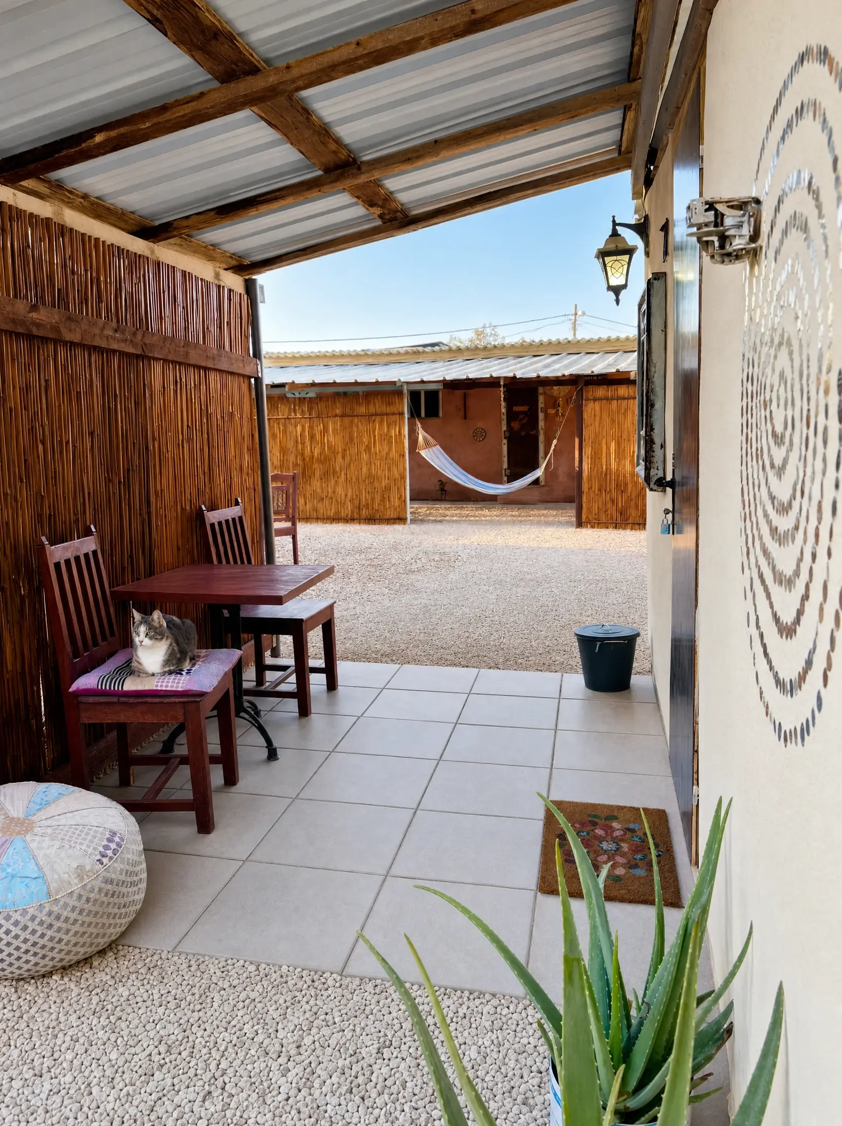 The Raz covered patio: a table, wooden chairs and a cat on a cushion, looking out to the yard and hammock