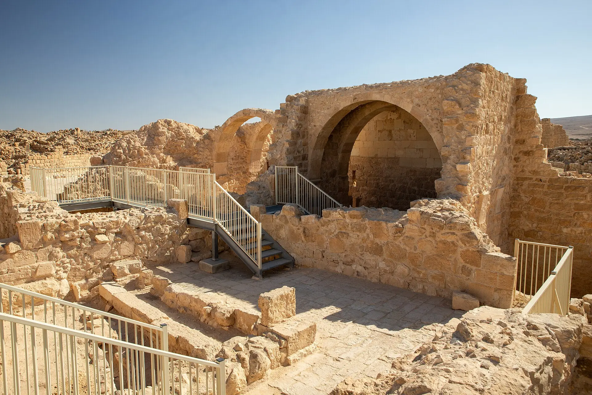 מבנה אבן עם קשת גדולה וחצר מרוצפת בגן לאומי שבטה, סמוך לבריכה שנחפרה